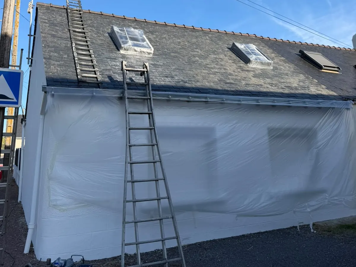 Façade de maison en cours de peinture, fenêtres et volets protégés par un film plastique, échelle en place